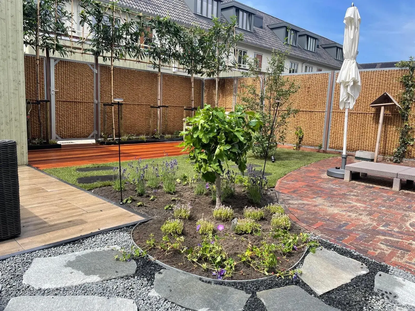 Eigen tuinproject met een ronde plantenborder, natuurlijke stapstenen, leibomen en een houten vlonder